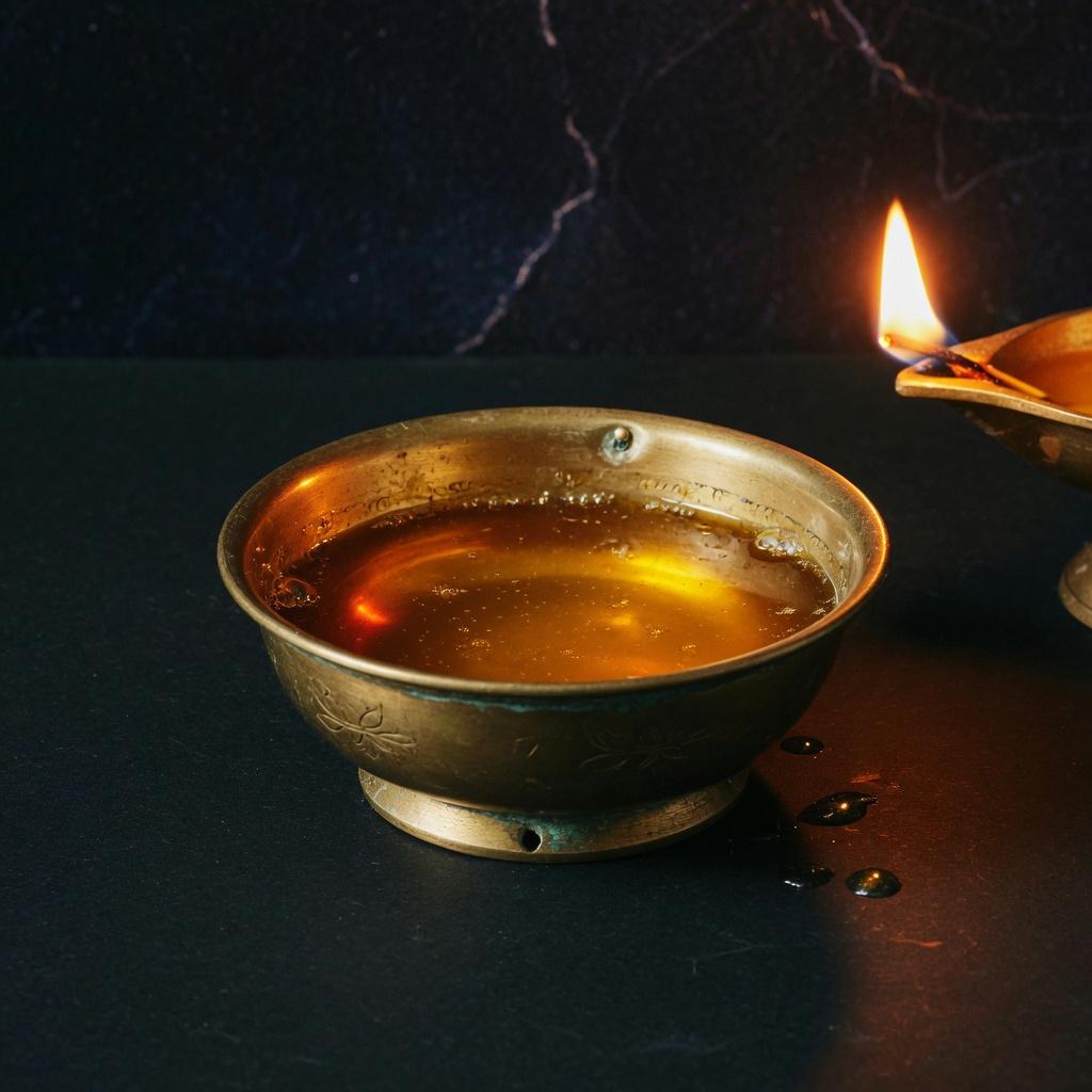A brass bowl of ghee in saffron lamp light