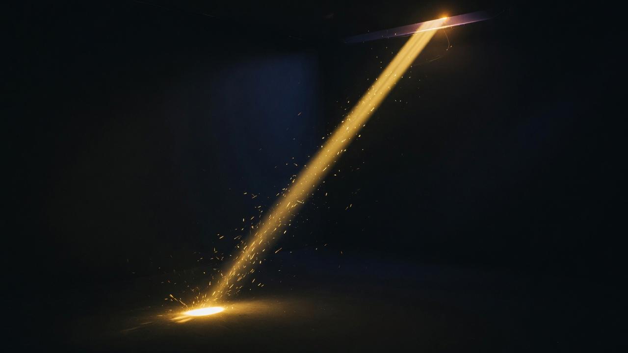 A single gold filament of light aimed through a dark room